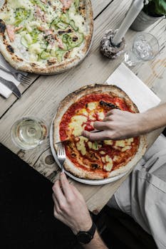 Overhead shot of hands slicing classic and gourmet pizzas on a rustic table, perfect for food lovers.