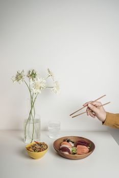 Stylish sushi setup with chopsticks, a flower vase, and two dishes on a minimalist table.