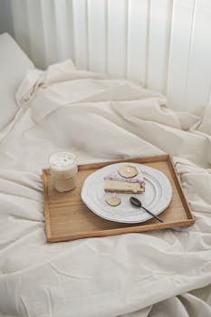 Slice of cake and iced coffee on a wooden tray, perfect breakfast in bed setting.
