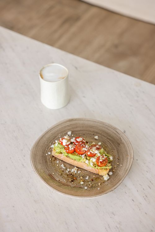 Free Avocado toast topped with cherry tomatoes and feta on a ceramic plate, perfect for a healthy breakfast. Stock Photo