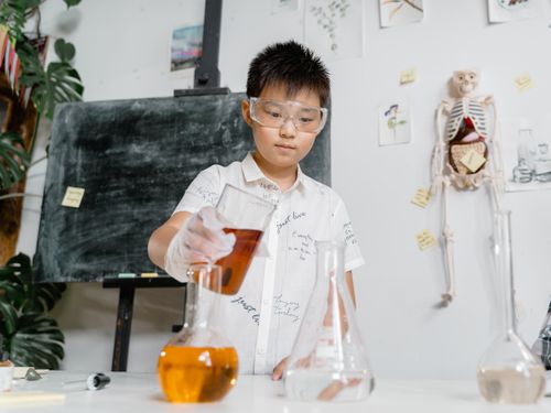 Free A child wearing goggles performs a chemistry experiment with colored liquids in a classroom. Stock Photo