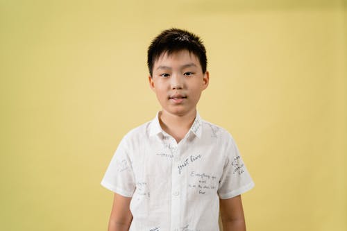 Boy in White Button Up T-shirt Standing Near Yellow Wall