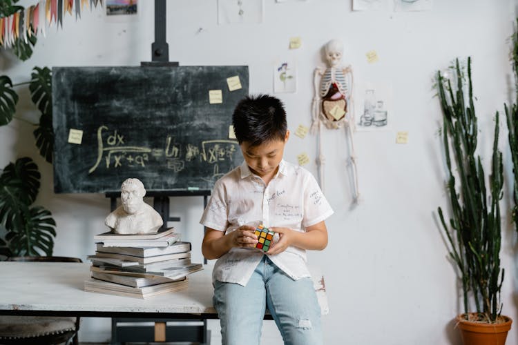 A Boy Sitting On The Table Solving A Rubik's Cube