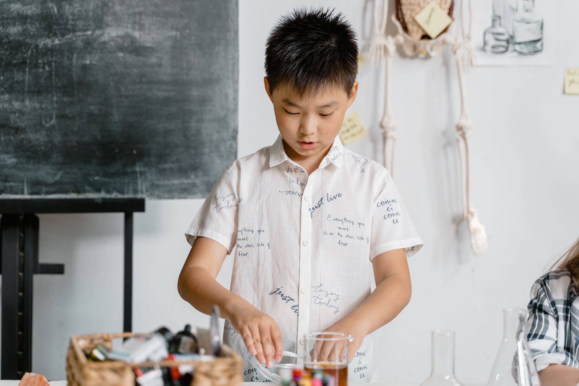 Boy in a classroom conducting a science experiment, wearing a white shirt.