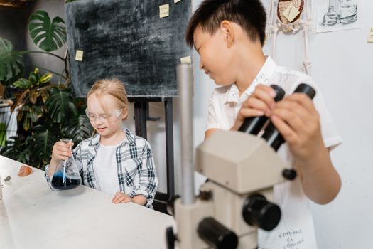Two children conducting a science experiment with a microscope and flask in a laboratory.