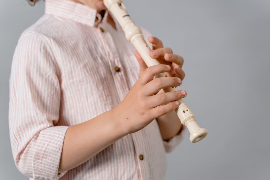 Child holding and playing a wooden recorder, close-up of hands and instrument.