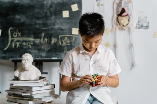 A Boy Playing with Rubik's Cube beside Stacked Books