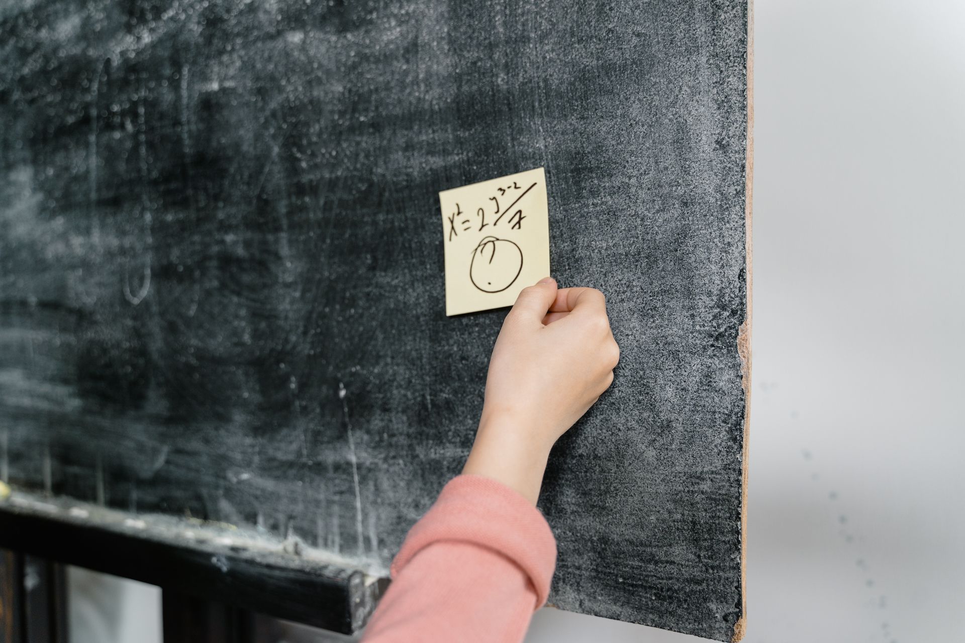 Close-up of a hand sticking a reminder note on a chalkboard in a classroom.