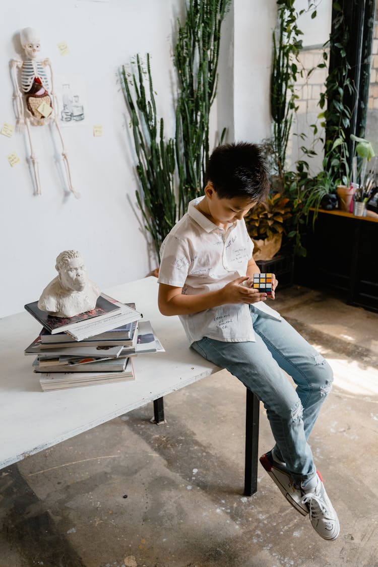 A Stack Of Books Beside A Boy Playing A Rubik's Cube