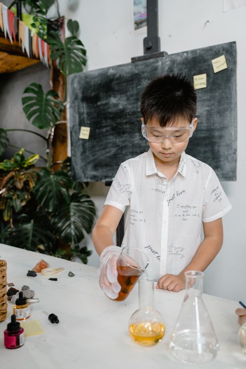 Free A young boy conducts a chemistry experiment in a classroom, focusing intently on mixing liquids. Stock Photo