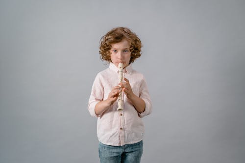 Free A Diligent Boy Playing His Flute on Gray Background Stock Photo