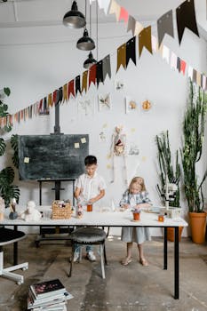 Two kids enthusiastically working on creative projects at a classroom table, surrounded by educational supplies.