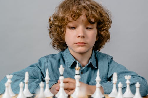 Close-Up Photo of a Serious Boy Looking at the White Chess Pieces