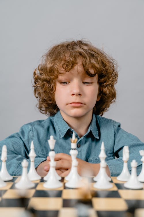 Close-Up Photo of a Serious Boy Looking at the White Chess Pieces