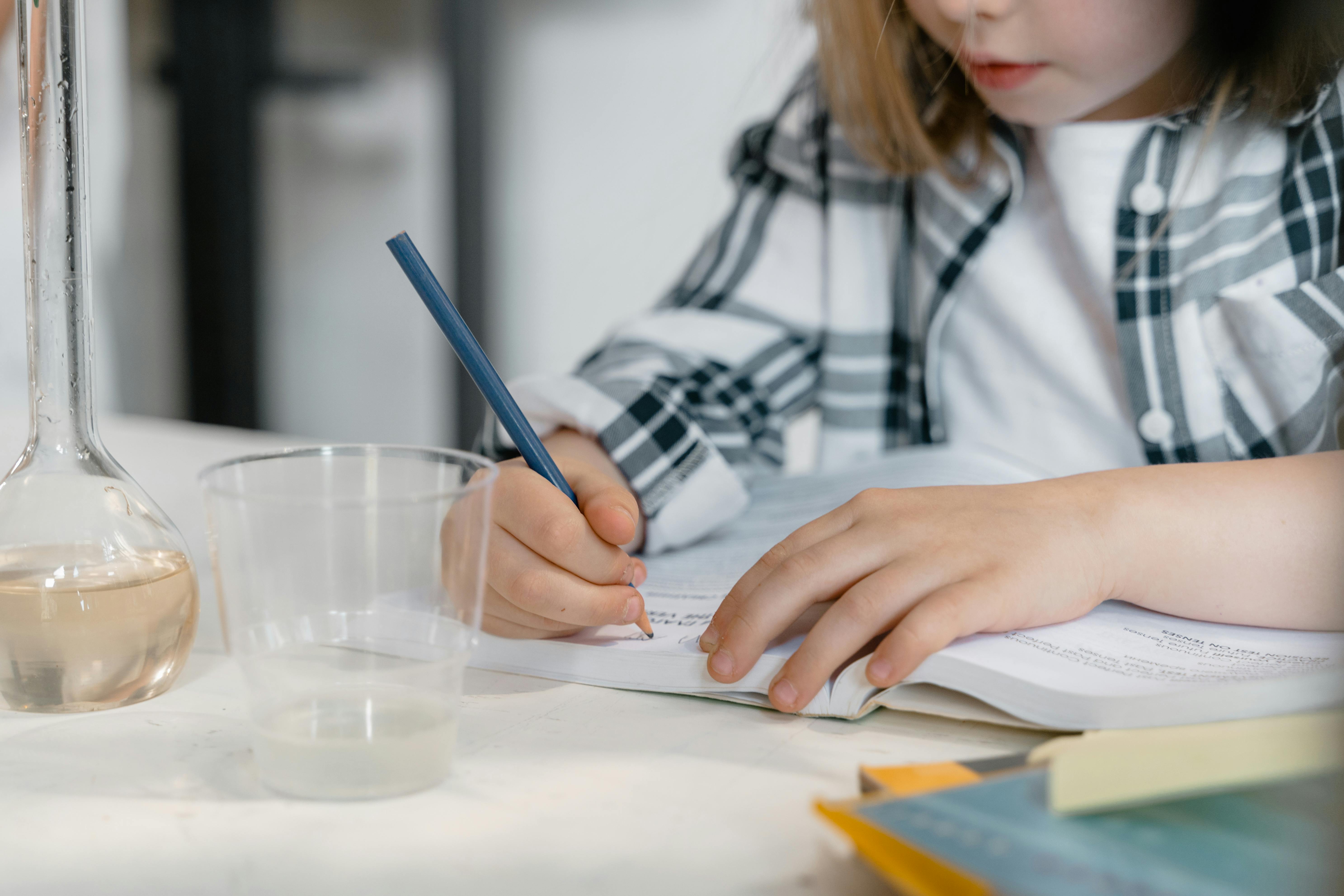 Young child learning science, writing surrounded by books and laboratory beaker.