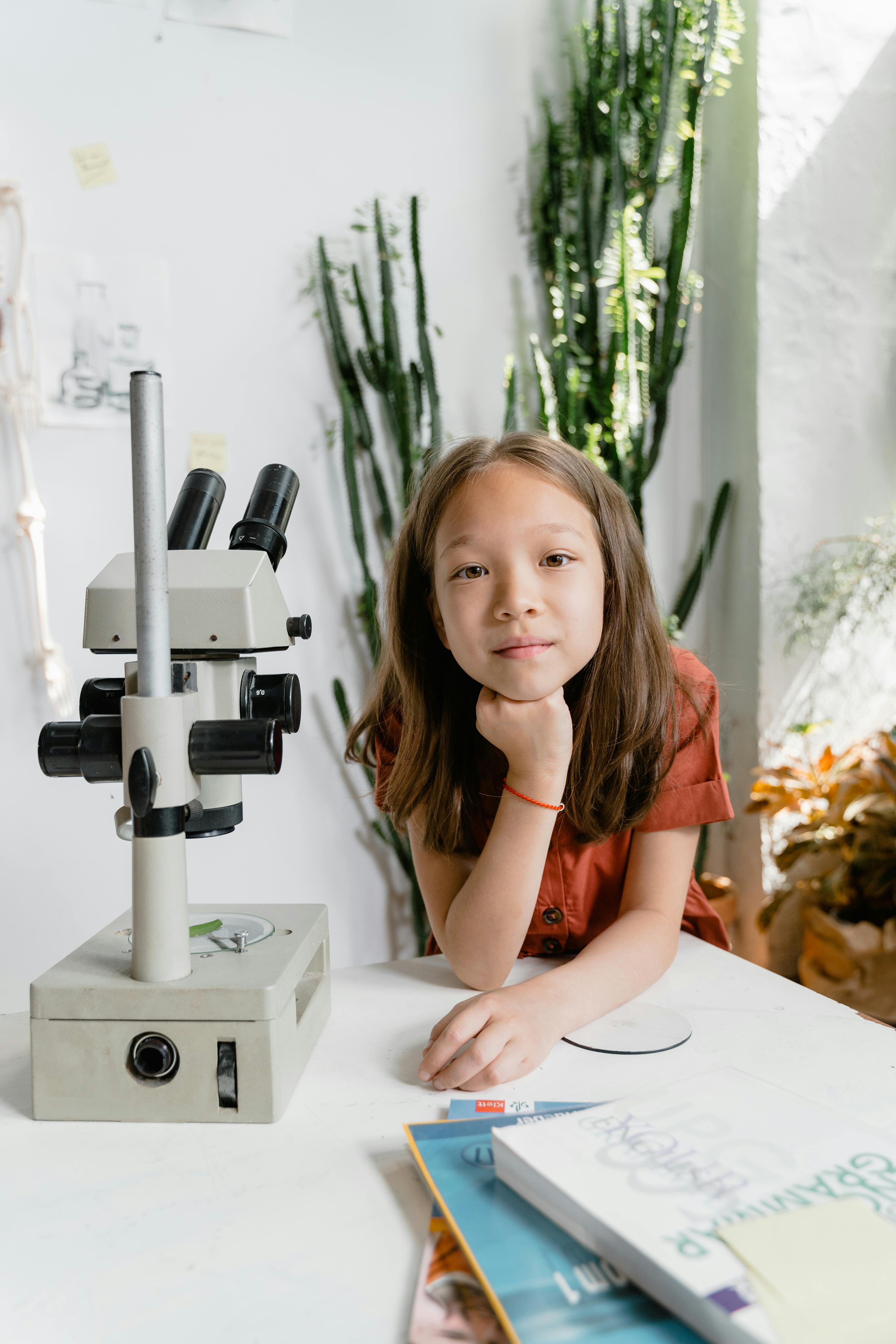 a girl posing on a table beside a microscope