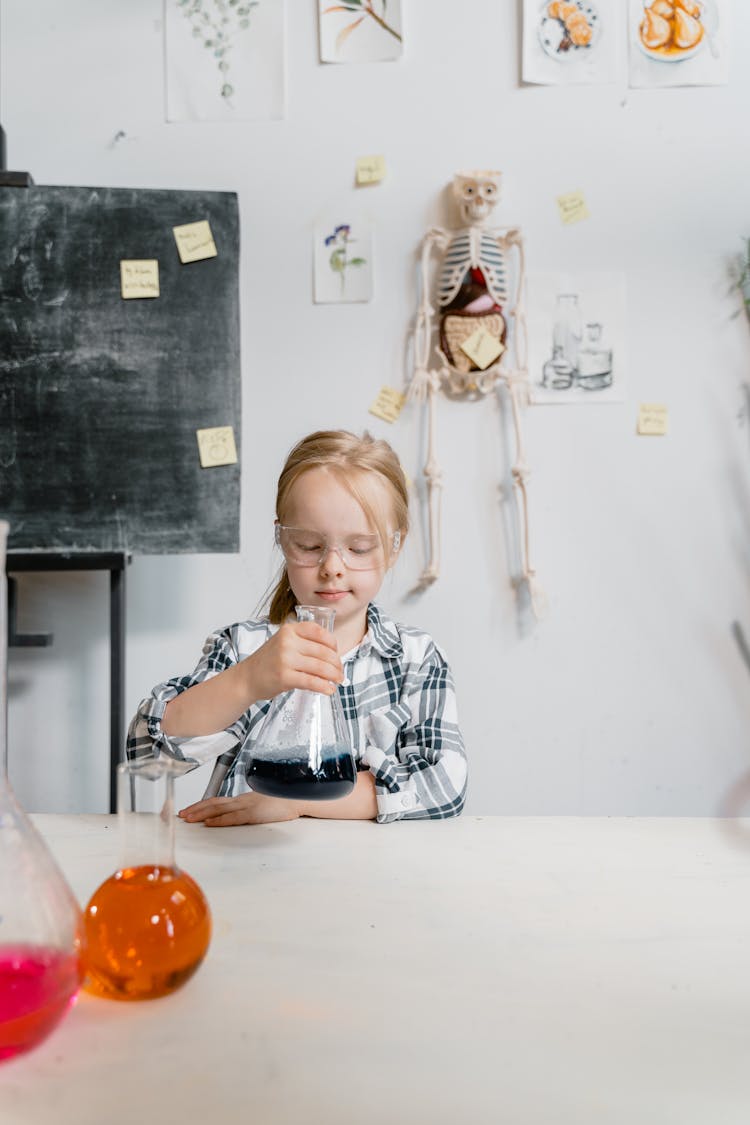 A Kid Wearing Safety Glasses While Looking At The Flask He Is Holding