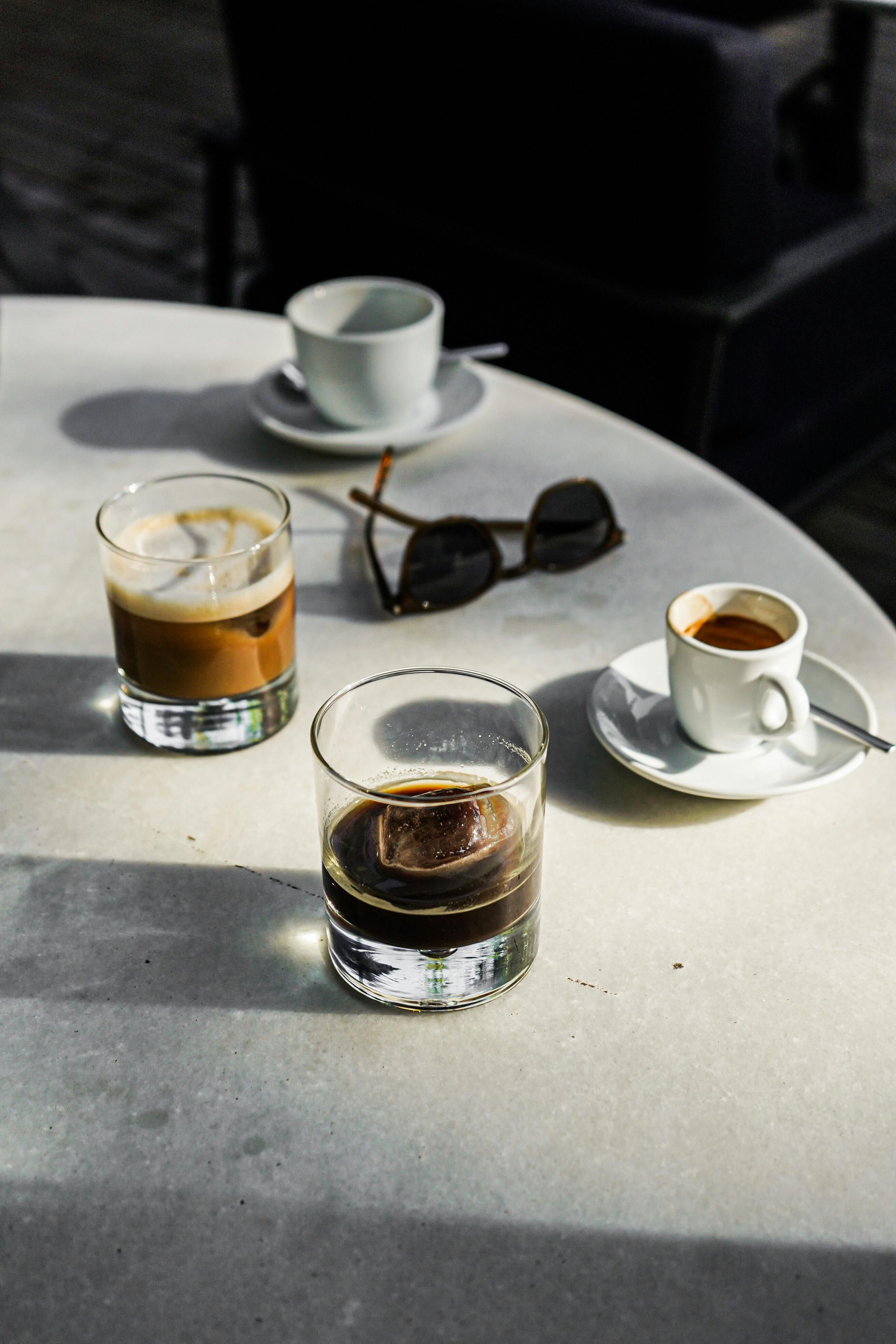 Variety of coffee drinks on a sunlit table with sunglasses, creating a stylish still life.