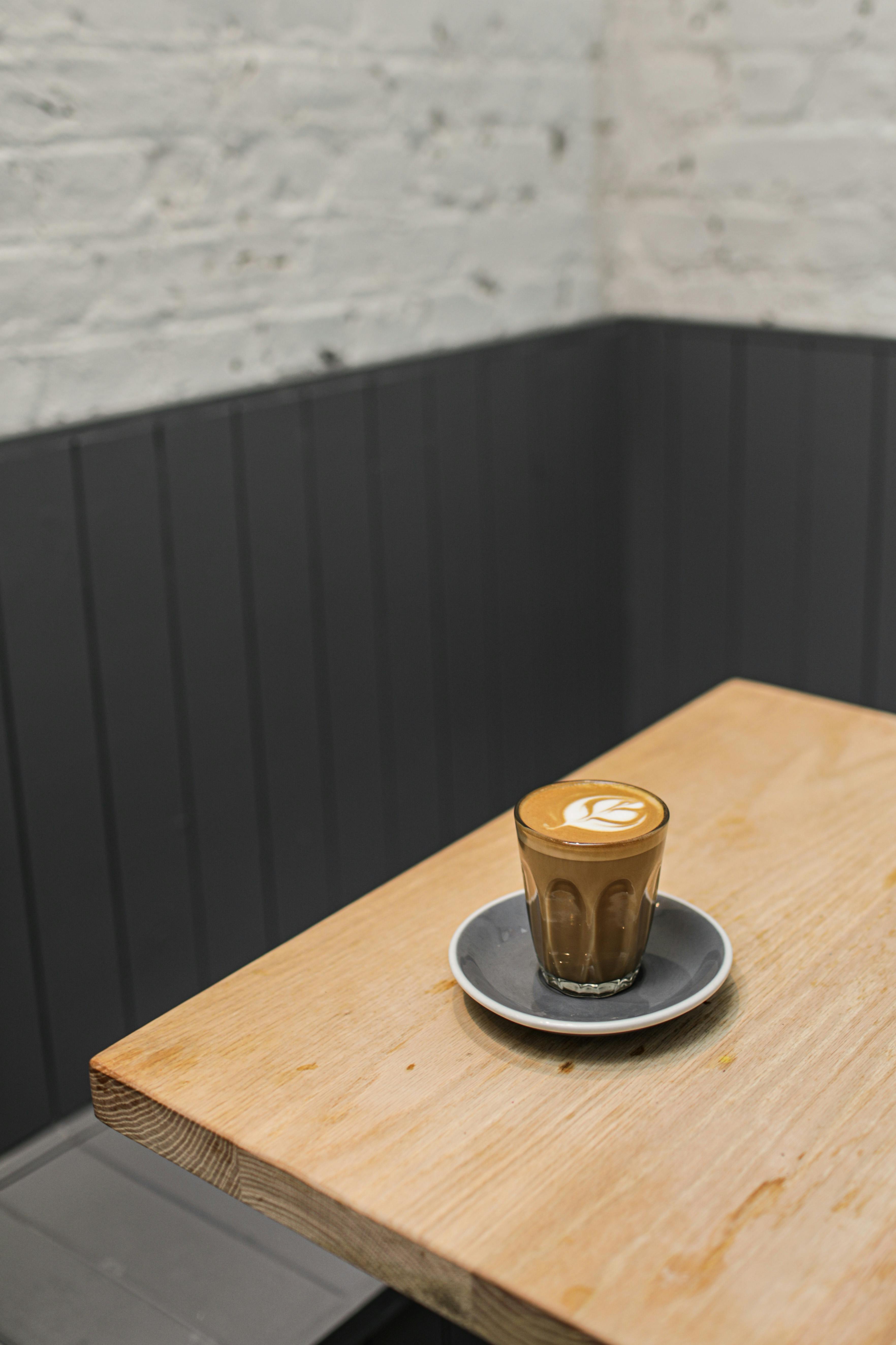 Free A beautifully crafted coffee latte with art on a wooden table in a cozy café setting. Stock Photo