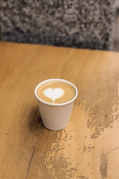 A cup of coffee with heart latte art served on a wooden table.