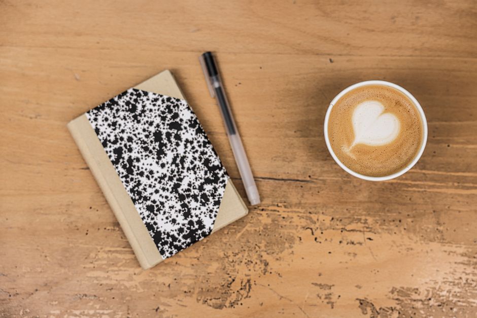 A comforting flatlay featuring a latte, marble notebook, and pen on a wooden table.