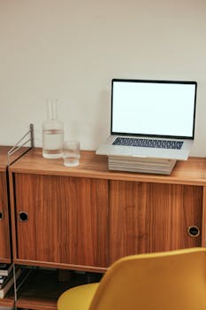 Minimalist workspace featuring a laptop on a wooden desk with a chair and glass carafe, ideal for productive work.