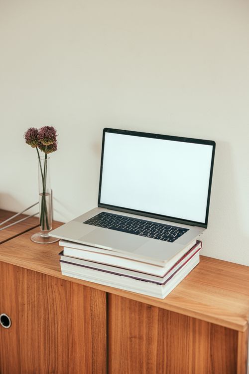 Free A sleek laptop sits atop a stack of books on a wooden desk, exuding modern minimalism. Stock Photo