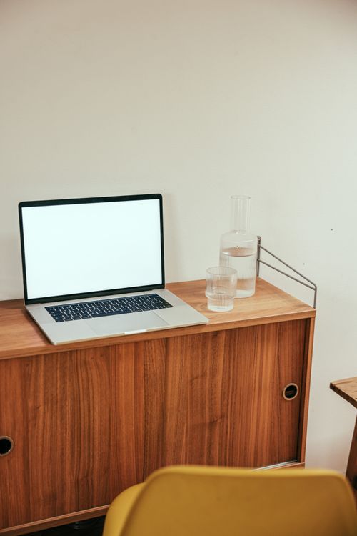 Free A clean and minimalist workspace featuring a laptop and glass of water on a wooden desk. Stock Photo