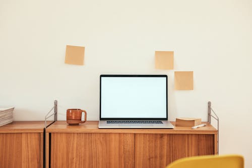 Wooden Table with Laptop and Cup of Coffee Near the Wall with Blank Sticky Notes