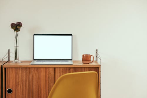 A Laptop on a Wooden Table Near White Wall