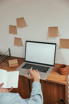 Adult working on laptop with notebook in minimal wooden desk setup.