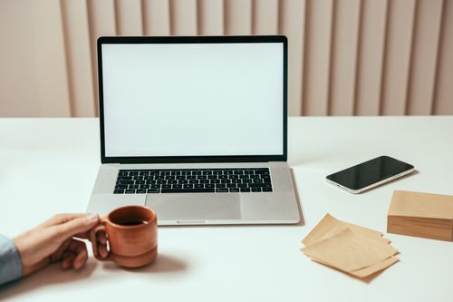 Free Minimalist workspace with laptop, smartphone, and coffee mug on a white desk. Stock Photo