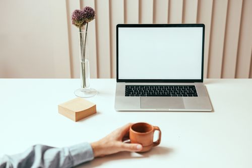 Free A minimalist workspace setup featuring a laptop, coffee mug, and decorative vase with flowers. Stock Photo