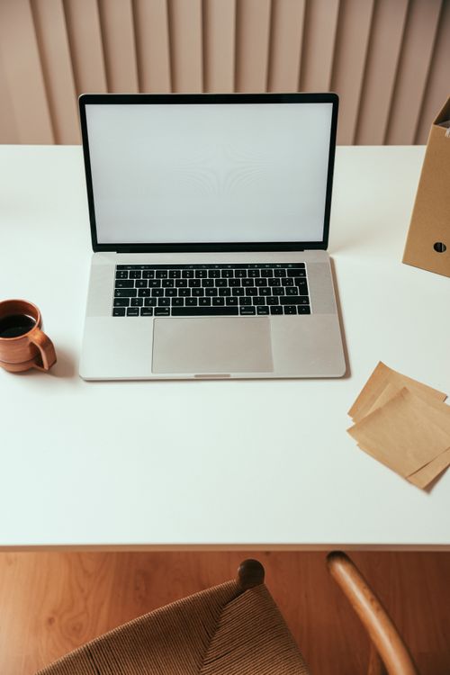 Free A minimalist workspace with a laptop, coffee cup, and paper on a white desk. Stock Photo