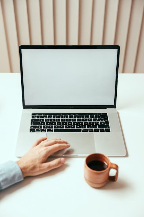 Person Using a Laptop Beside a Cup of Coffee