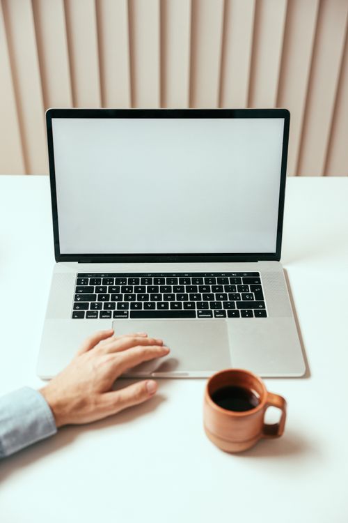 Free A clean and modern workspace featuring a laptop, coffee mug, and a person’s hand. Stock Photo