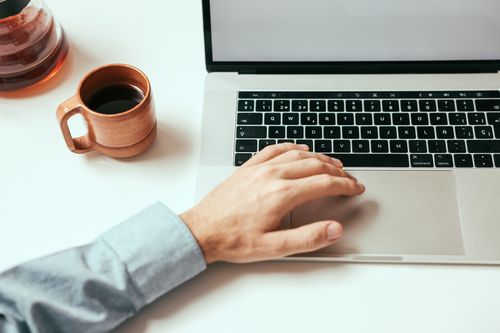 Free A close-up of a hand on a laptop touchpad with coffee, depicting a productive workspace. Stock Photo