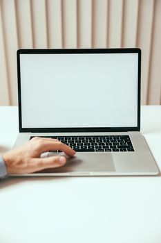 A hand touching a laptop with a blank screen, ideal for mockup designs in a modern setting.