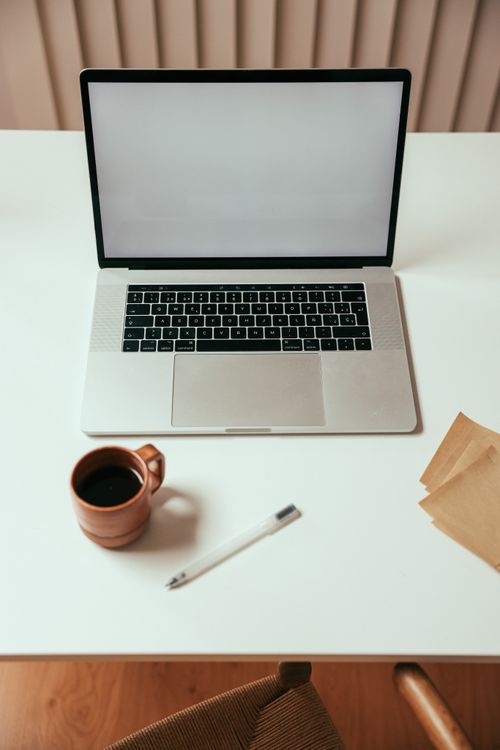 Free Top view of a modern workspace with a laptop, coffee cup, pen, and papers on a white table. Stock Photo