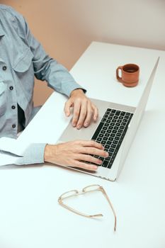 Adult typing on a laptop at a minimalist desk with a cup of coffee.