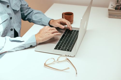 Free Adult working remotely on laptop with eyeglasses and cup on a white table. Stock Photo