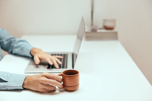 A Person Holding a Cup While Using a Laptop