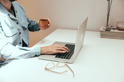Free Adult working remotely on a laptop with coffee, showcasing a relaxed work environment. Stock Photo
