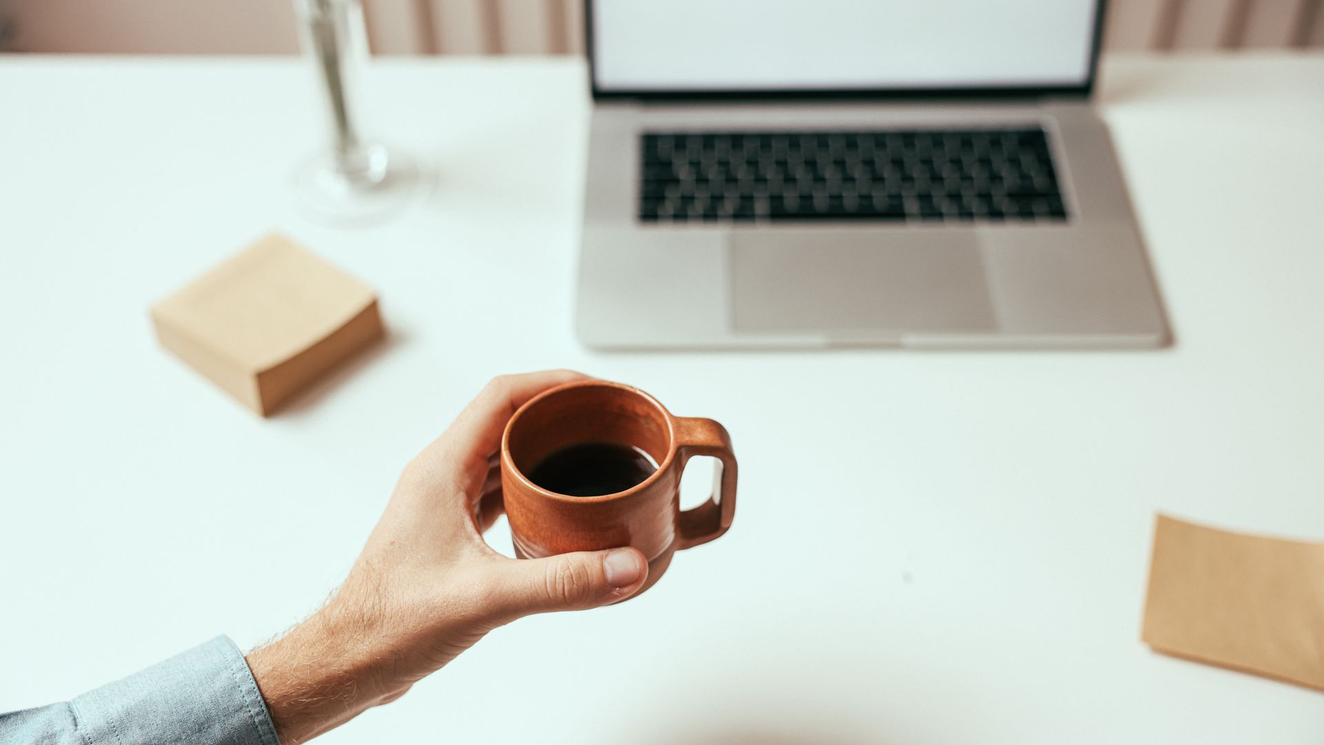 Nootropics for Work Performance: Enhance Your Productivity A person holds a brown coffee cup near a laptop on a clean white desk, perfect for remote work themes — nootropics for work performance