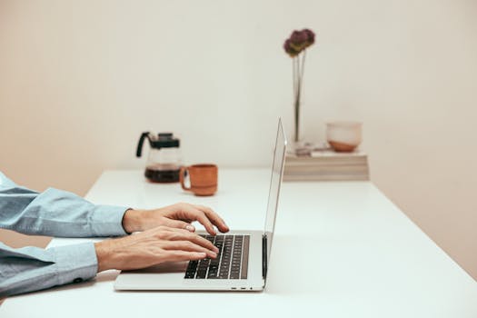 Hands typing on a laptop in a stylish home office, symbolizing modern remote work lifestyle.