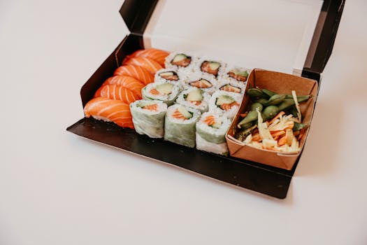 A mouth-watering sushi platter featuring fresh salmon, rolls, and vegetables in a to-go box.