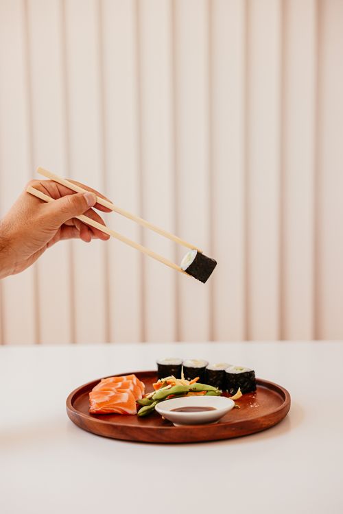 Free A hand holding sushi with chopsticks over a wooden plate with sushi and sashimi. Stock Photo