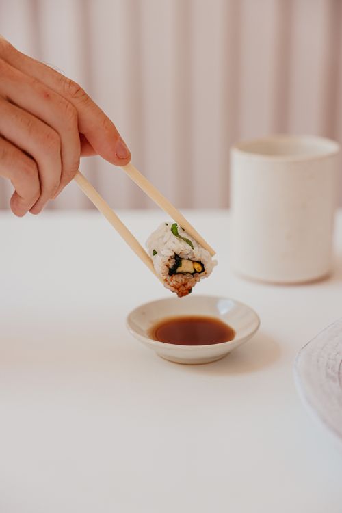 Free A hand delicately dips a sushi roll into soy sauce using chopsticks, depicting Japanese cuisine beautifully. Stock Photo