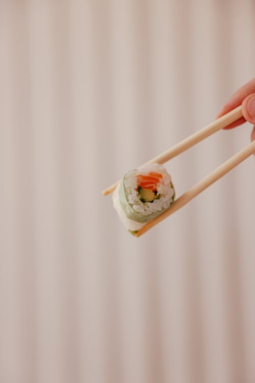 Person Using Chopsticks Holding a Sushi