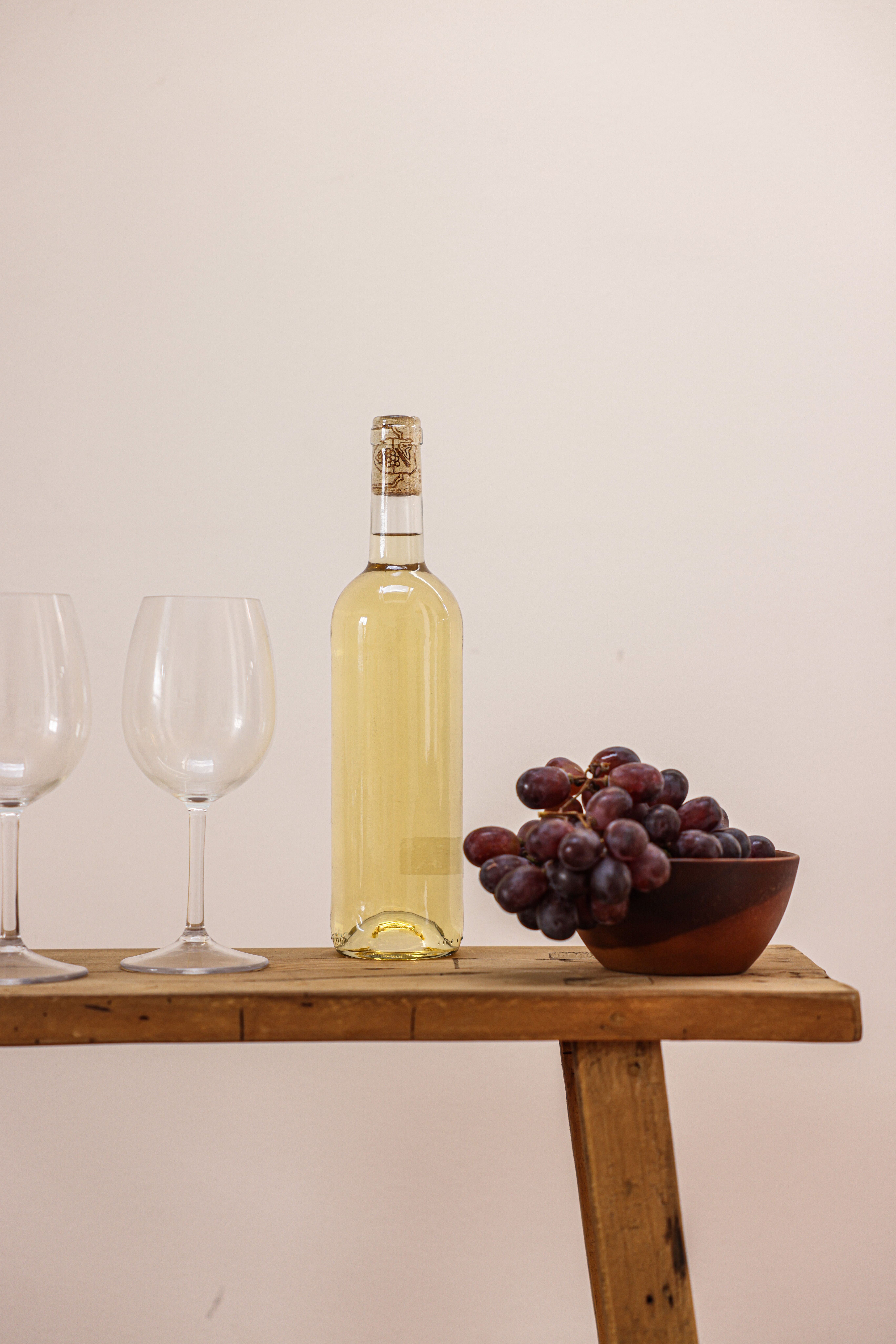 Bottle of white wine beside a bowl of grapes on a wooden bench